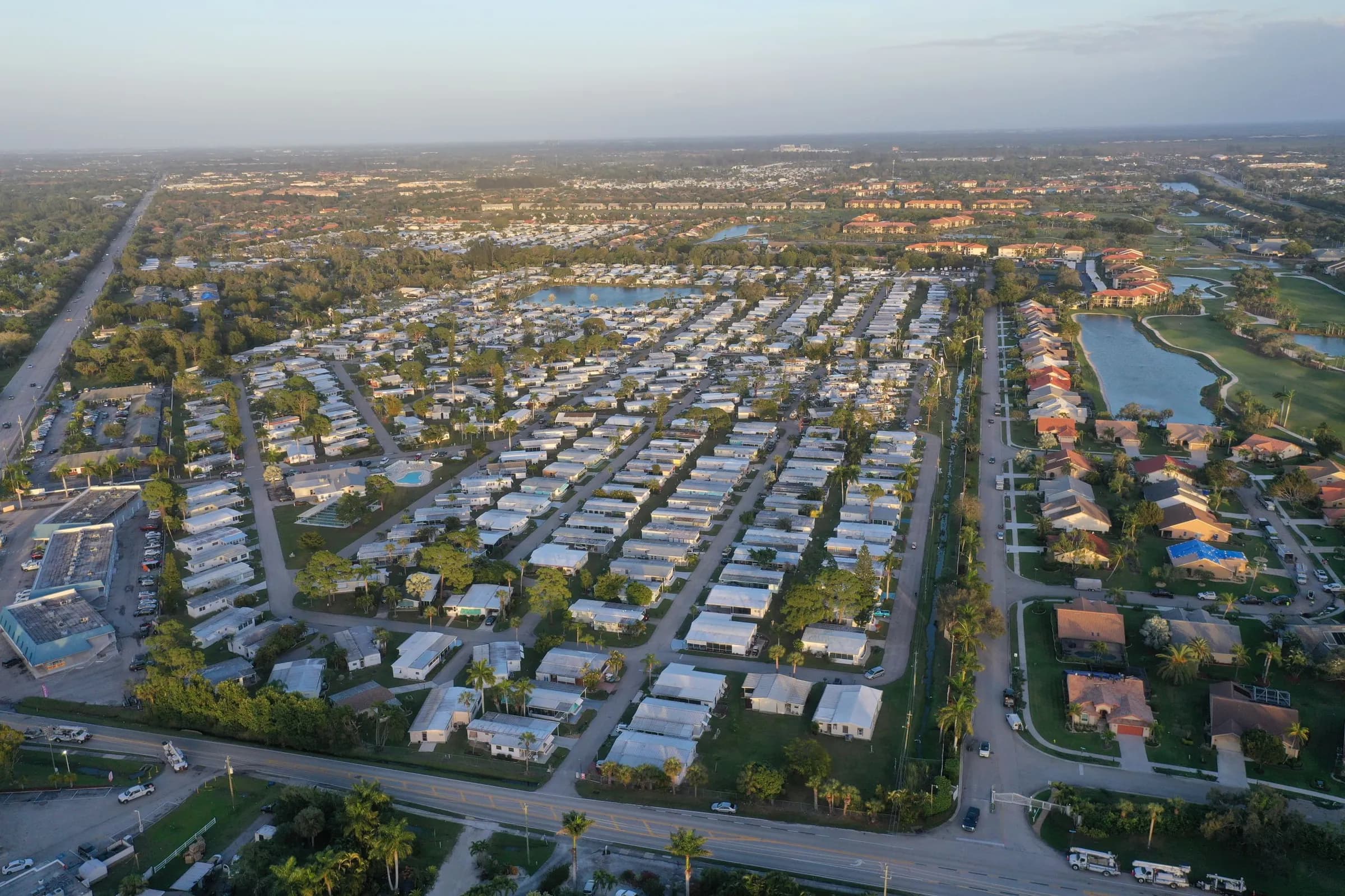 Aerial view of a Fort Myers, Florida neighborhood with rows of low-rise homes, tree-lined streets, a lake and a golf course under a clear sky.